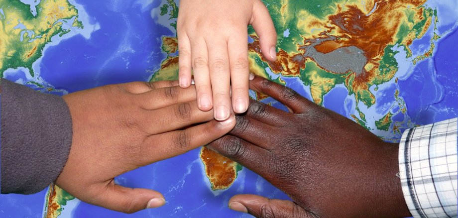 Drei Hände in unterschiedlen Hautfarben werden über die Weltkarte gehalten.