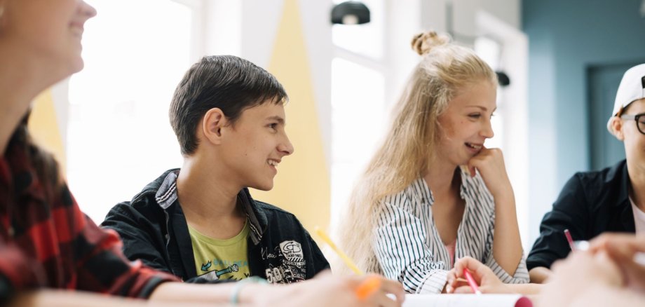 Schüler:innen sitzen gemeinsam an einem Tisch und tauschen sich aus.