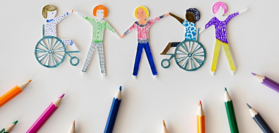Ausgeschnittene Papierfiguren von Kindern, darunter liegen Buntstifte.