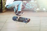 Unterkörper einer Person, die zusammen mit ihrem Skateboard in die Lüfte springt.