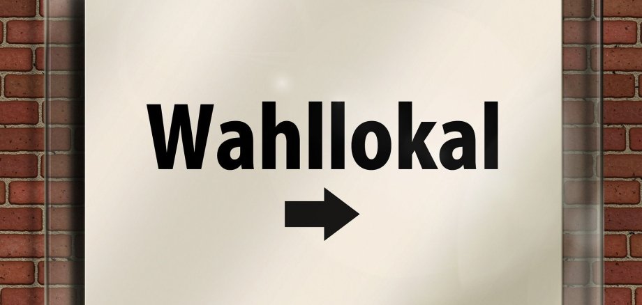 Ein Schild an einer Hauswand mit der Aufschrift "Wahllokal" und einem Pfeil nach rechts.