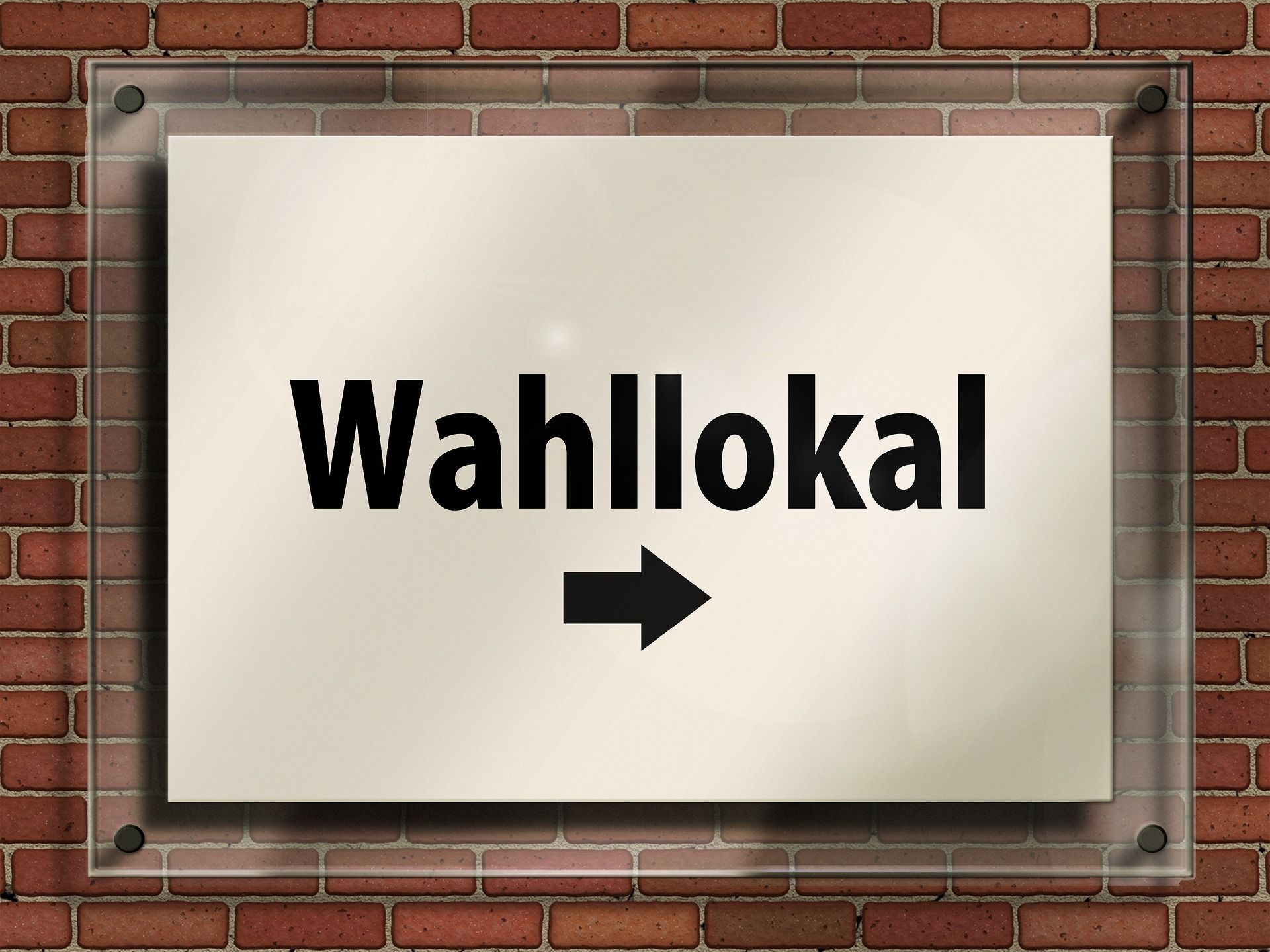 Ein Schild an einer Hauswand mit der Aufschrift "Wahllokal" und einem Pfeil nach rechts.