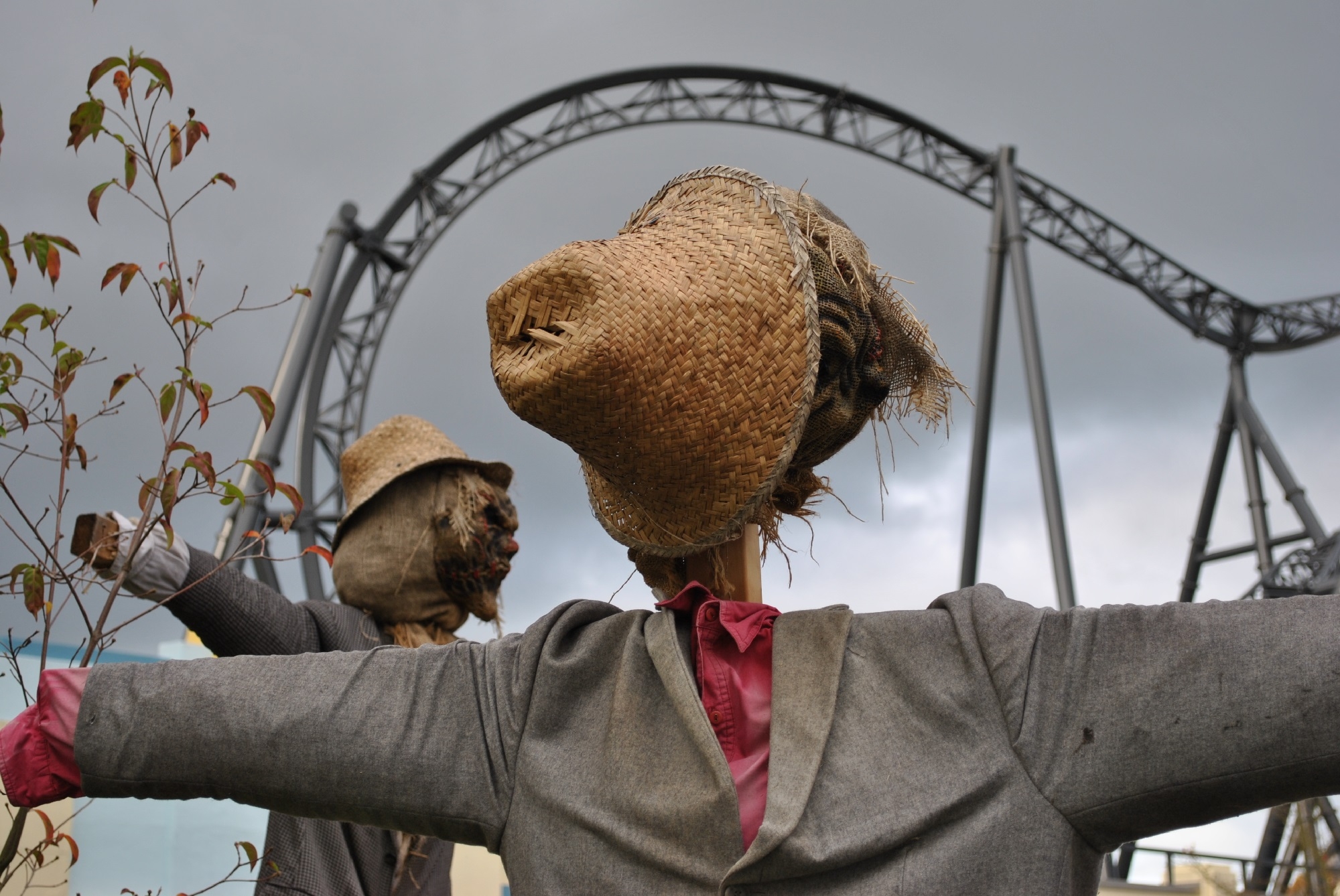 Mann sieht eine Achterbahn im Movie Park Bottrop und davor stehen zwei angezogene Vogelscheuchen aus Stroh. Es ist Herbst.