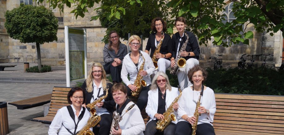 Das Foto zeigt ein Saxophon Ensemble teilweise auf einer Bank sitzend vor einer Kirche.