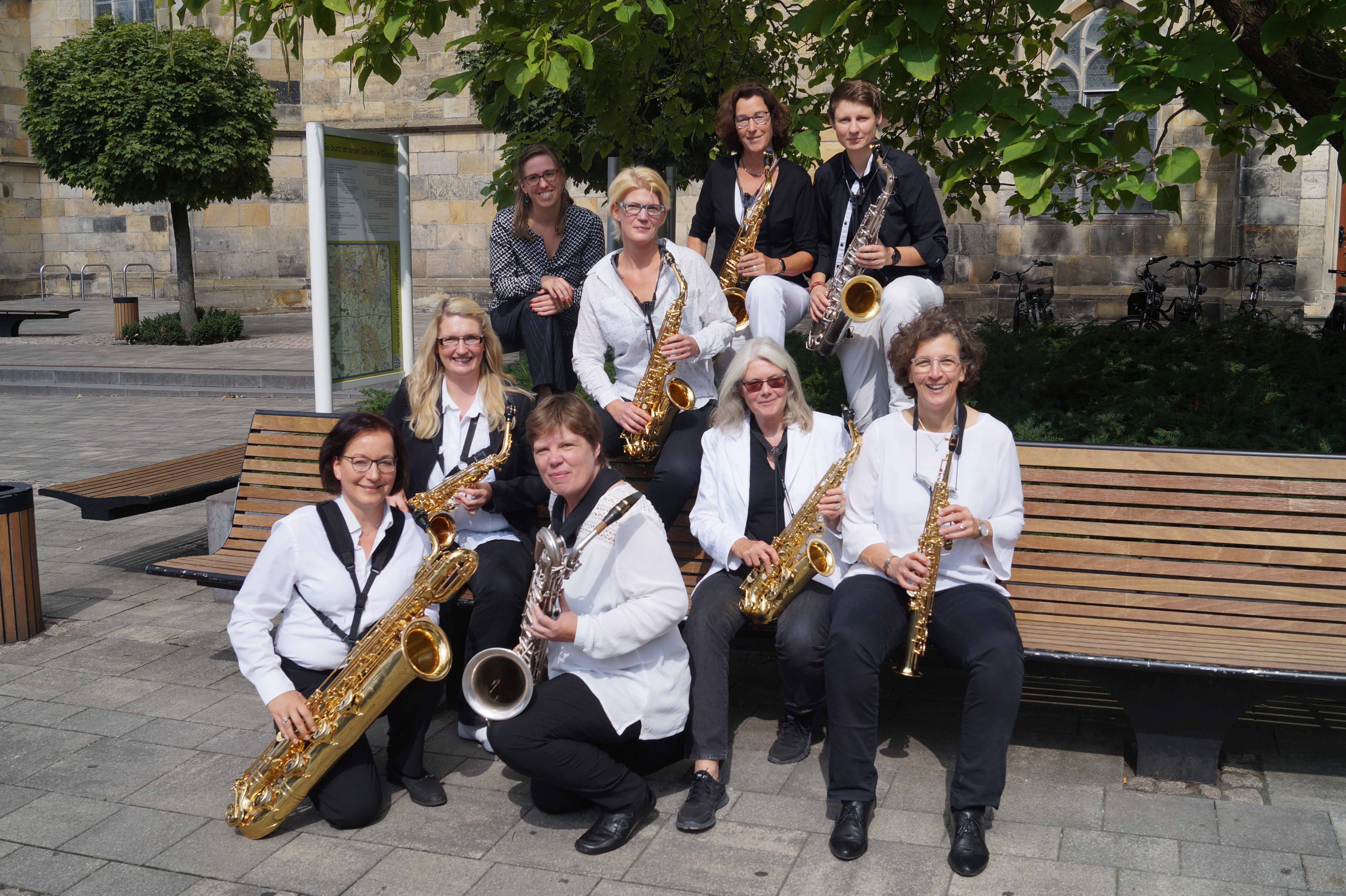 Das Foto zeigt ein Saxophon Ensemble teilweise auf einer Bank sitzend vor einer Kirche.
