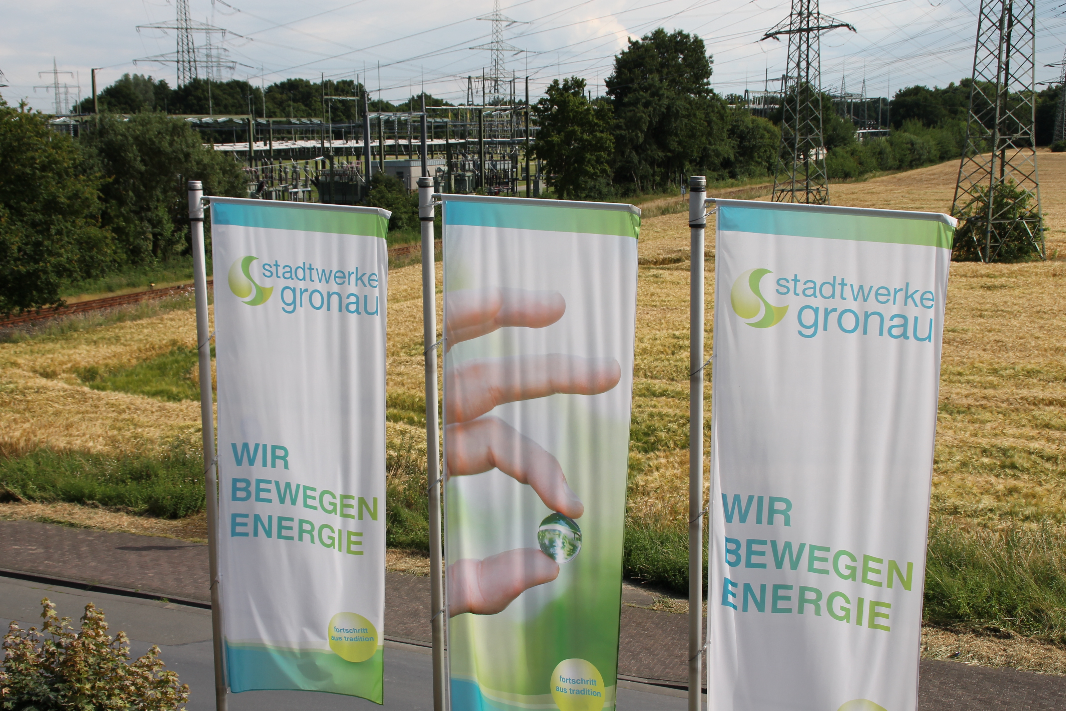 Das Bild zeit drei Flaggen der Stadtwerke, die vor einer Wiese hängen.