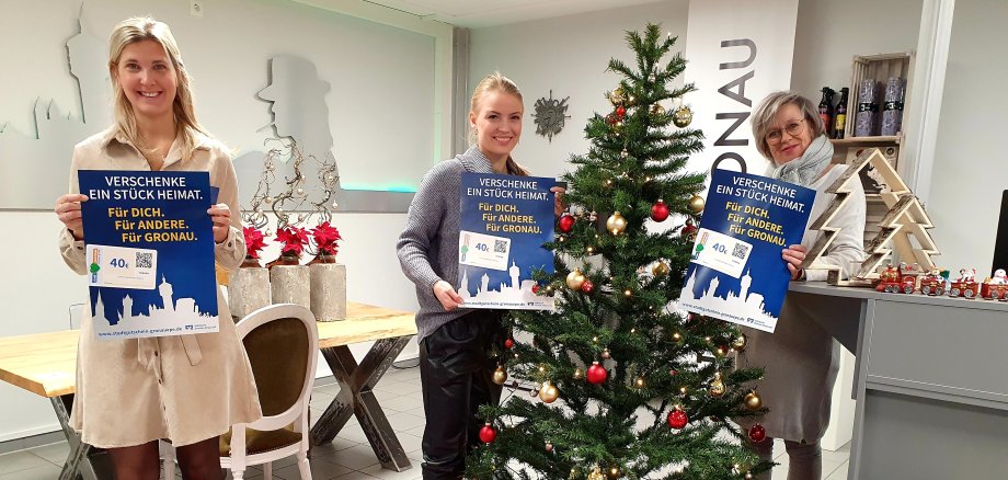 Bild zeigt 3 Mitarbeiterinnen neben einem Weihnachtsbaum mit Gutscheinen in der Hand