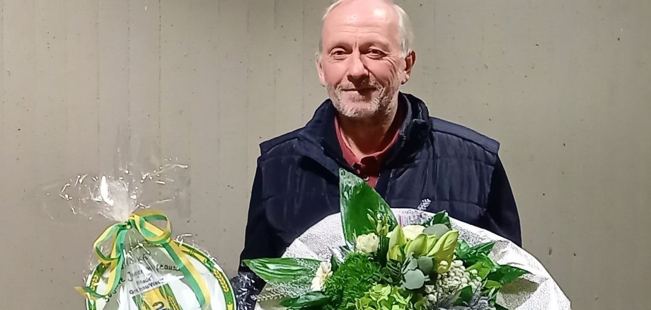 Sie sehen Wolfgang Lobjinski mit einem Blumenstrauß und dem Ehrenteller der Stadt Gronau
