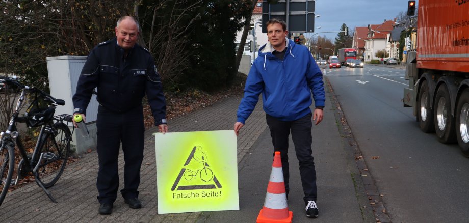 Sie sehen zwei Männer mit einem Hinweisschild gegen Geisterradler