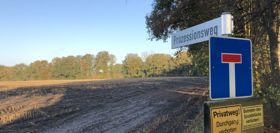 Sie sehen ein Straßenschild und dahinter ein freies Gelände