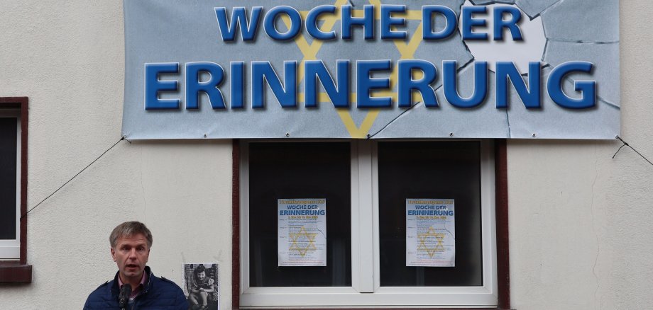 Sie sehen Bürgermeister Rainer Doetkotte vor der Synagoge Epe mit dem Plakat zur Woche der Erinnerung