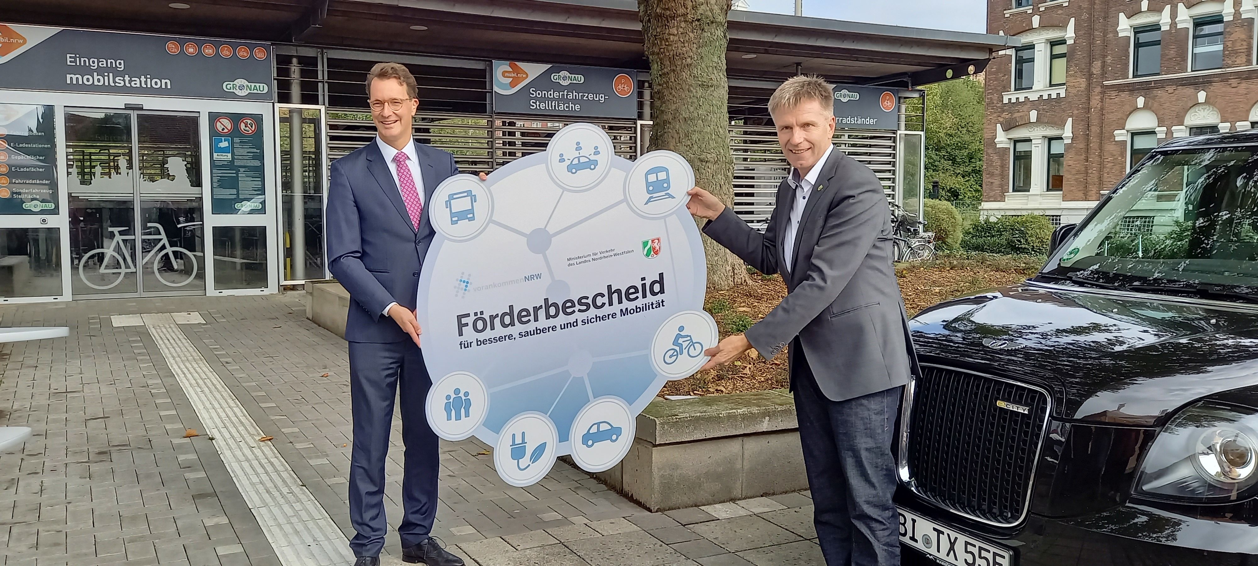 Verkehrsminister Wüst und Bürgermeister Doetkotte vor der Mobilstation in Gronau