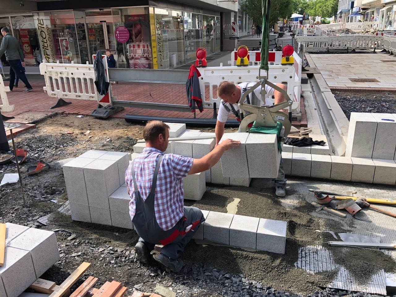 Zwei Mitarbeiter setzen einen Stein für den Gronaubrunnen. 