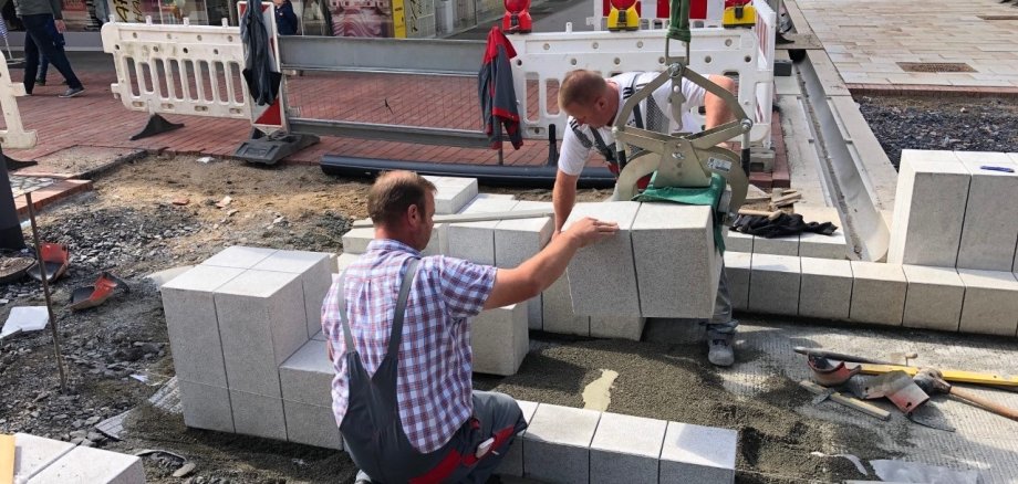 Zwei Mitarbeiter setzen einen Stein für den Gronaubrunnen. 