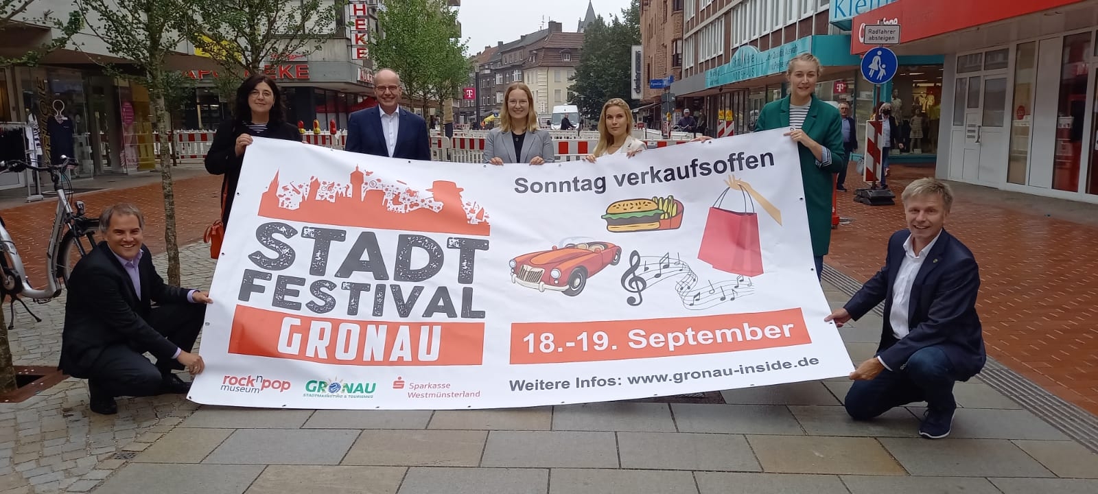 Alle Beteiligten freuen sich auf das Stadtfest und halten das Plakat zum Stadtfest hoch.