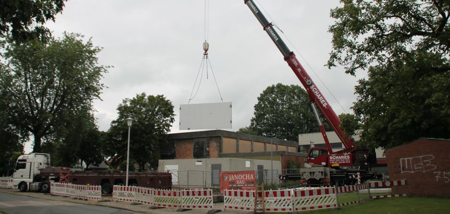 Der Schwerlastkran hebt ein Wandteil hoch über die Baustelle.