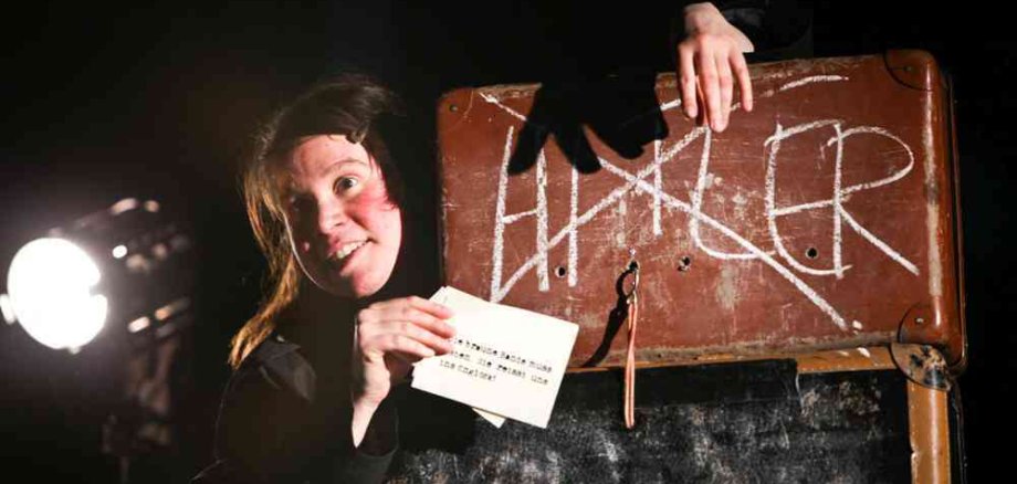 Eine Frau steht auf der Bühne vor einem Schild auf dem der Name Hitler durchgestrichen ist.