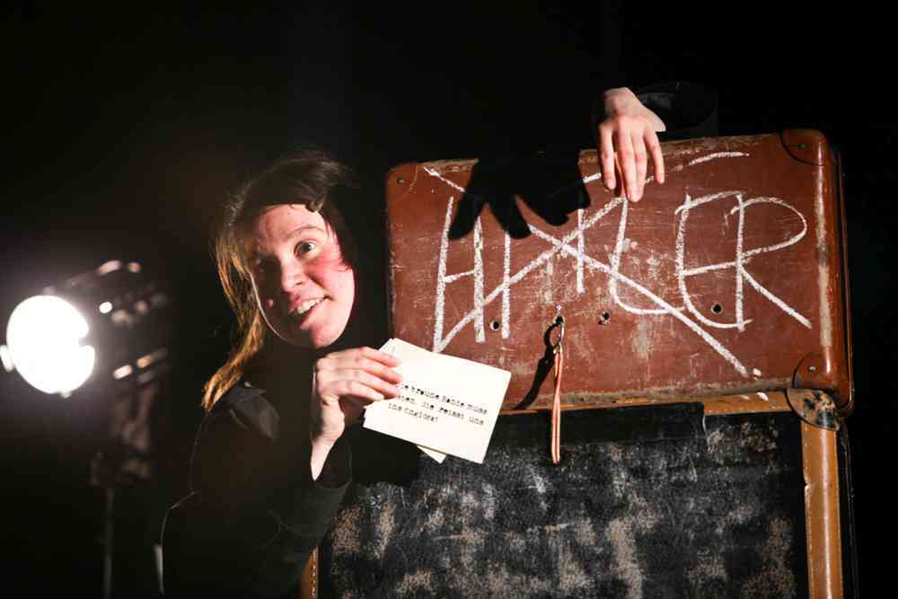 Eine Frau steht auf der Bühne vor einem Schild auf dem der Name Hitler durchgestrichen ist.