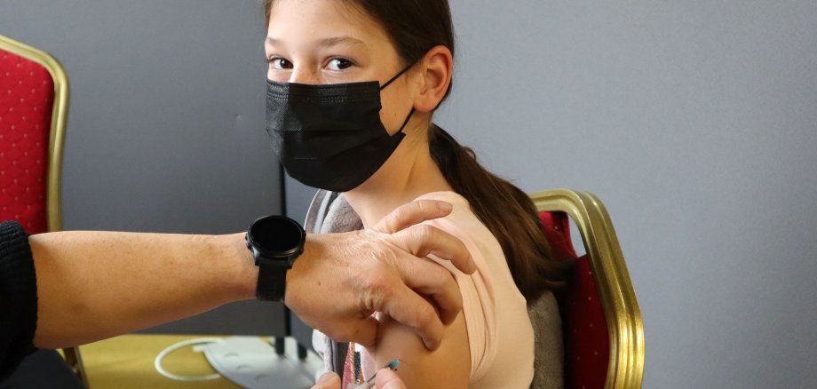 Kind mit Mundschutz bekommt eine Impfspritze