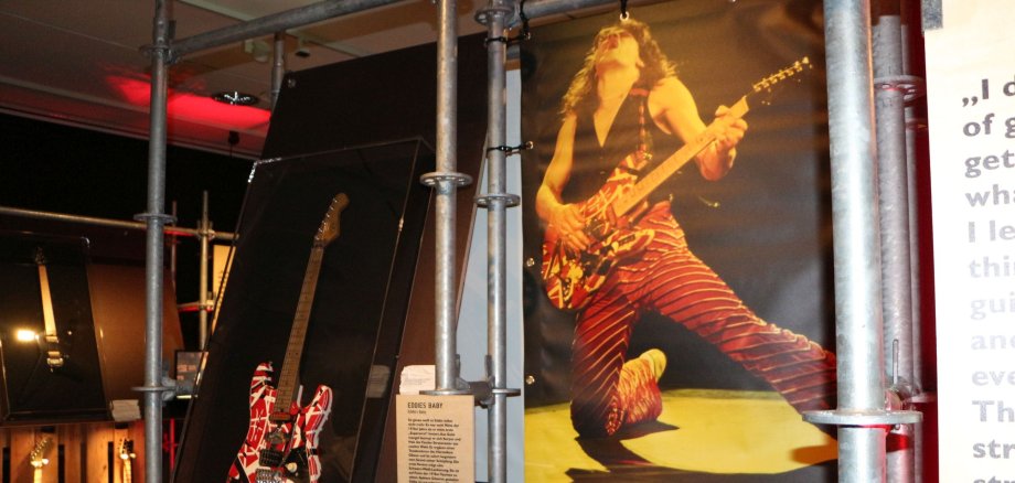 Ein van Halen Plakat in der Ausstellung. Daneben hängt eine Gitarre.
