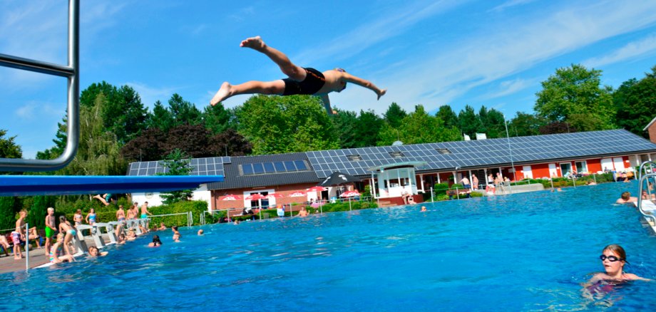 Ein Mann springt von einem 1-Meter-Brett in das Becken des Freibades.