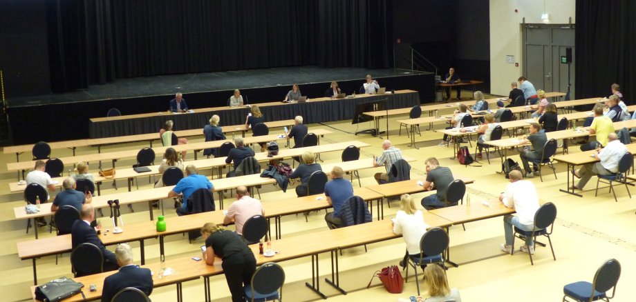 Die Auftaktveranstaltung in der Bürgerhalle: Mehrere Bürgeri*innen sitzen an Tischen und schauen zur Bühne.