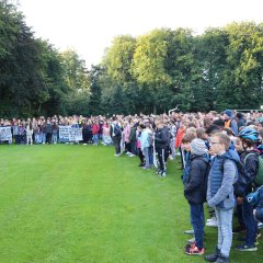 Zahlreiche Schüler*innen lauschen der Ansprache auf der Bühne.