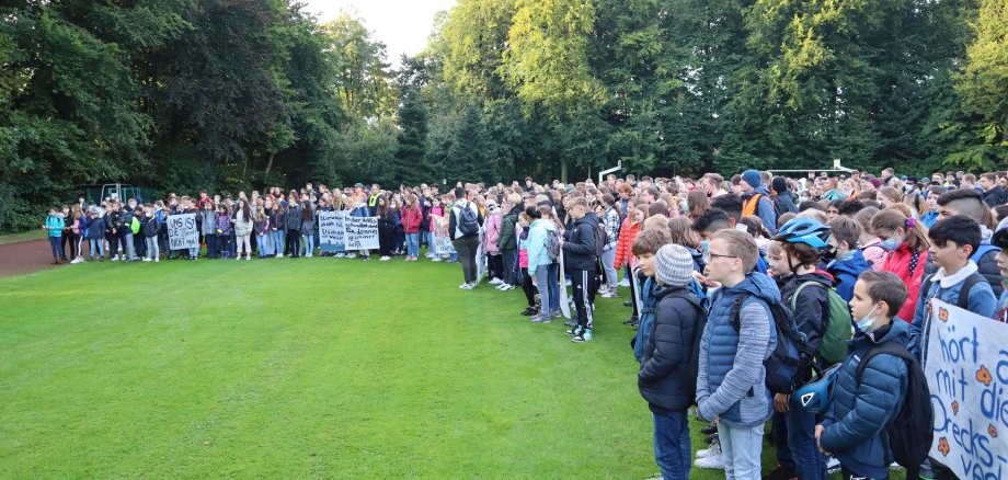 Zahlreiche Schüler*innen lauschen der Ansprache auf der Bühne.