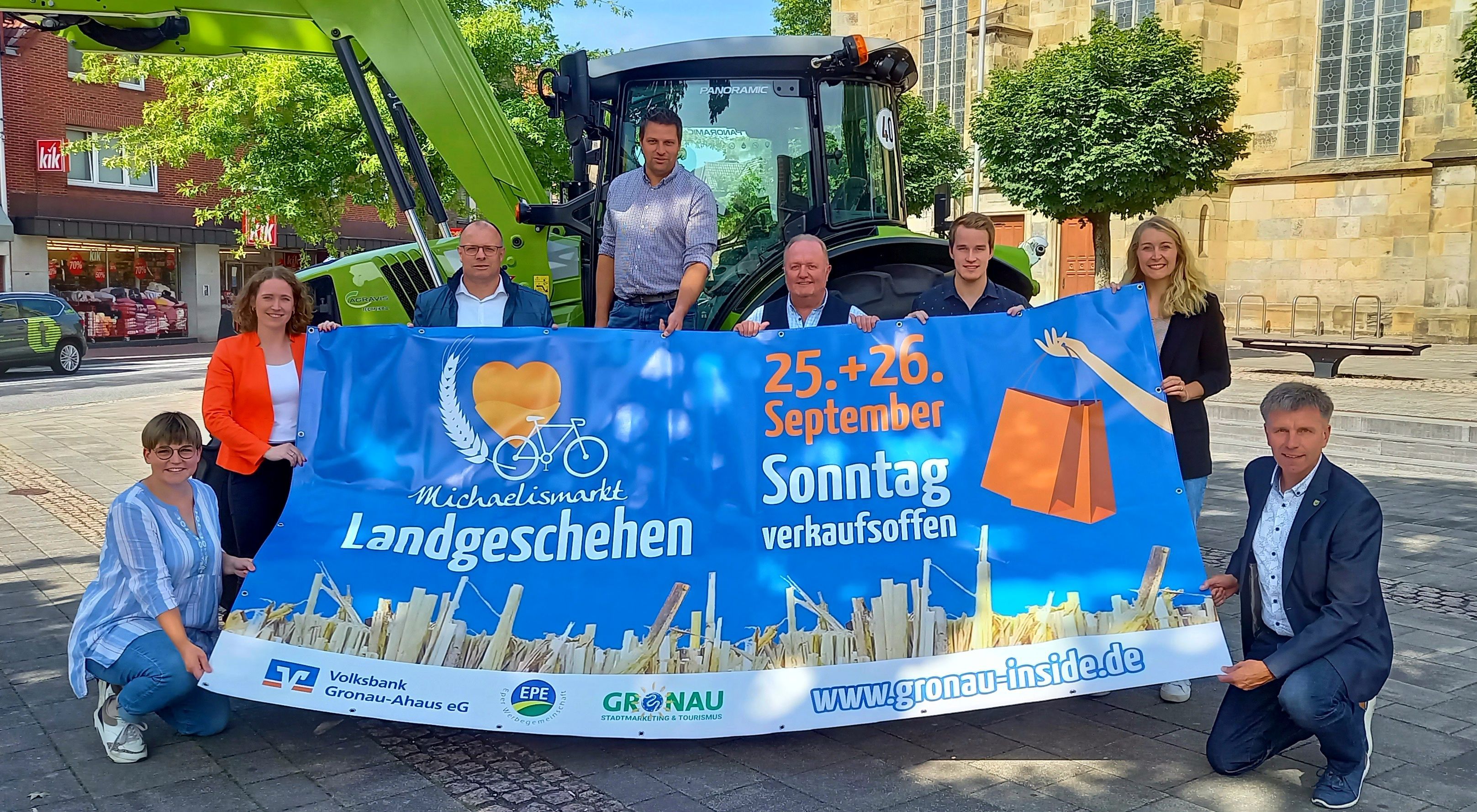 Alle beteiligten Organisator*innen freuen sich auf die Veranstaltung und halten das Banner hoch. Im Hintergrund ist ein Trecker zu sehen.