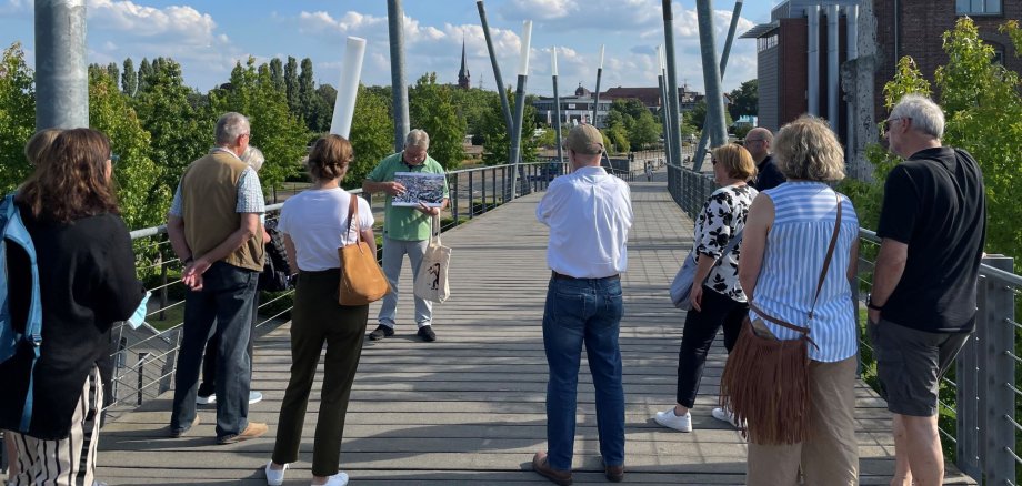 Mehrere Gäste hören Klaus Wiedau bei einer Stadtführung zu.