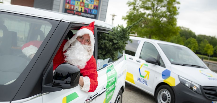 Der Weihnachtsmann sitzt mit einem Tannenbaum im G-Mobil.