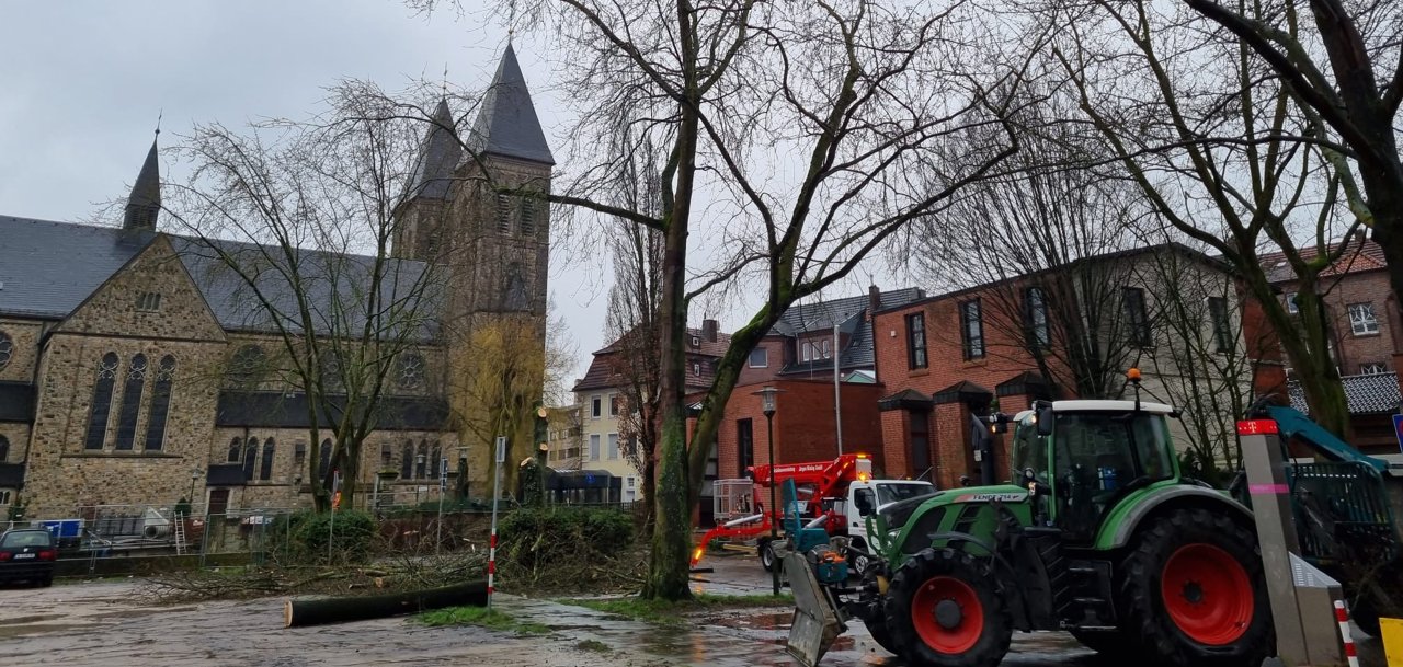 Auf der Parkplatzfläche in der Bahnhofstraße liegen abgesägte Äste. Daneben steht ein Trecker sowie ein Hubsteiger.