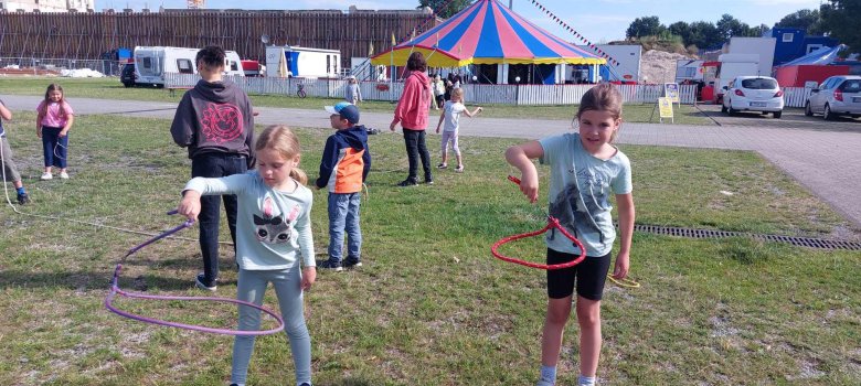Eine Gruppe Kinder übt mit dem Lasso vor dem Zirkuszelt.