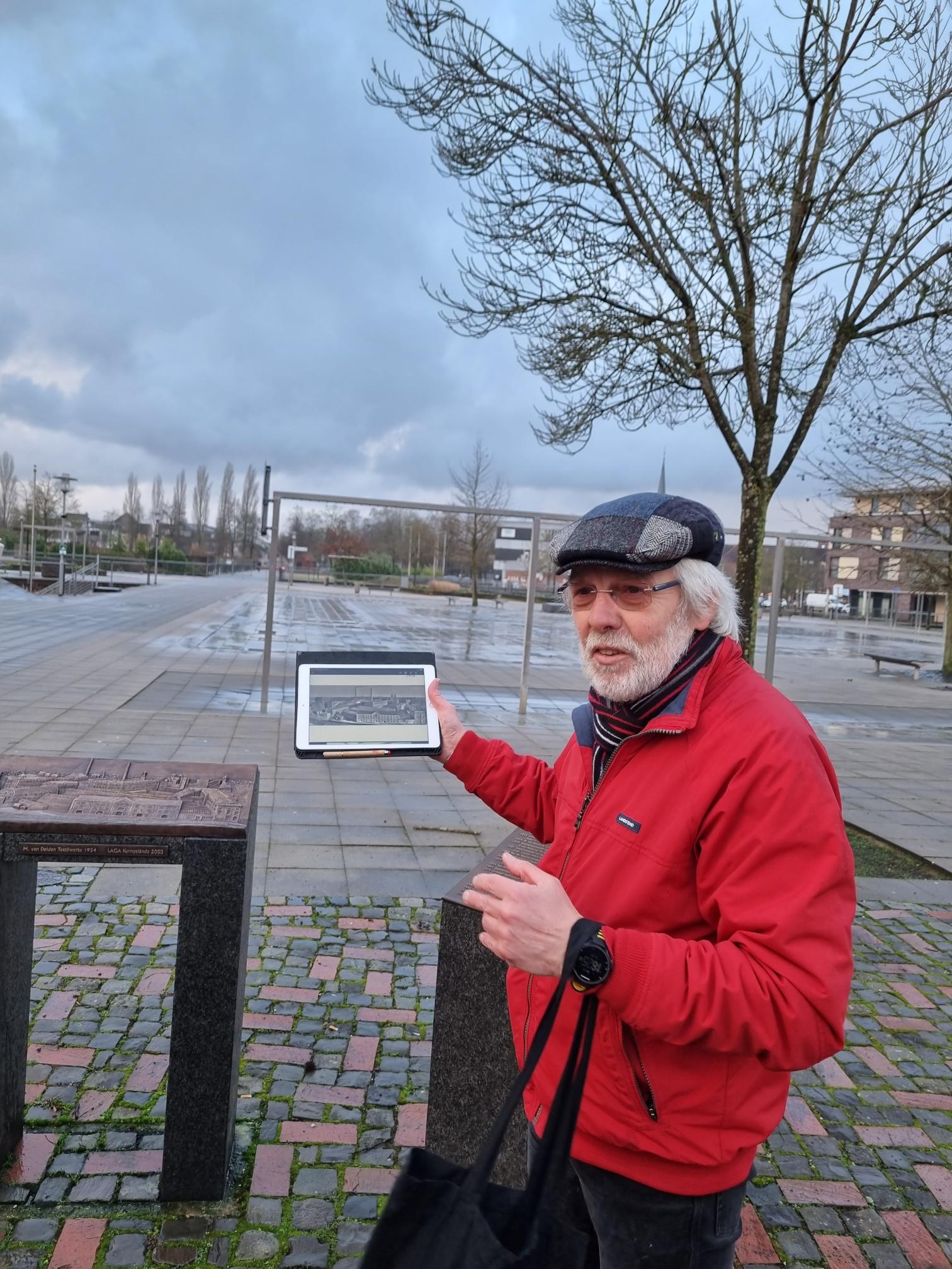 Günter Poggemann hält ein Tablet in der Hand und erzählt etwas dazu.