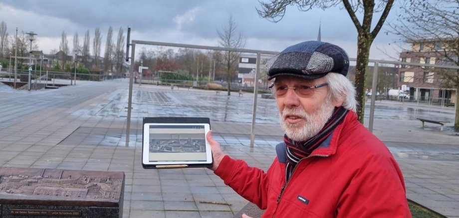 Günter Poggemann hält ein Tablet in der Hand und erzählt etwas dazu.