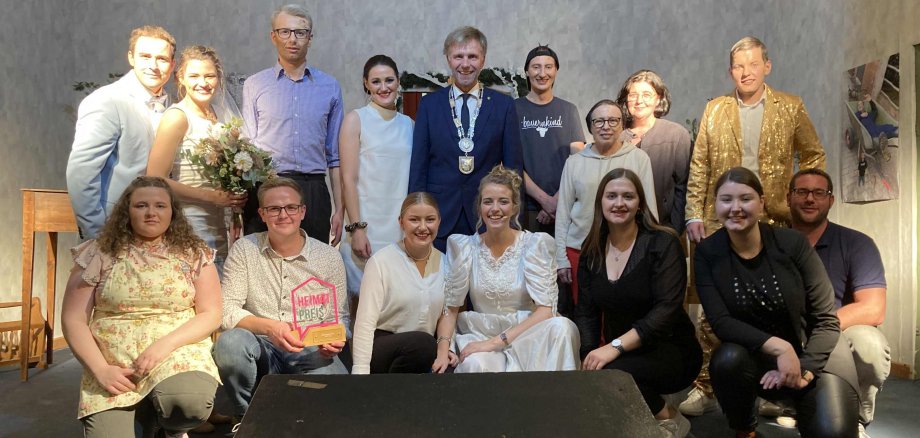 Bürgermeister Rainer Doetkotte (im Bild mit Bürgermeister-Kette) überreicht den Heimatpreis 2022 an die Theater-Gruppe der KLJB. Dazu fanden sich die Beteiligten auf der Bühne zu einem Gruppenfoto zusammen.