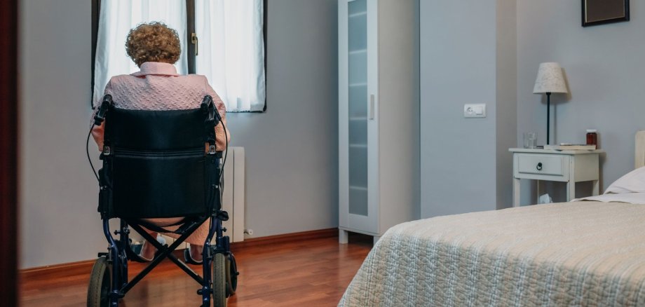 Eine Seniorin in einem Rollstuhl alleine in einem Raum