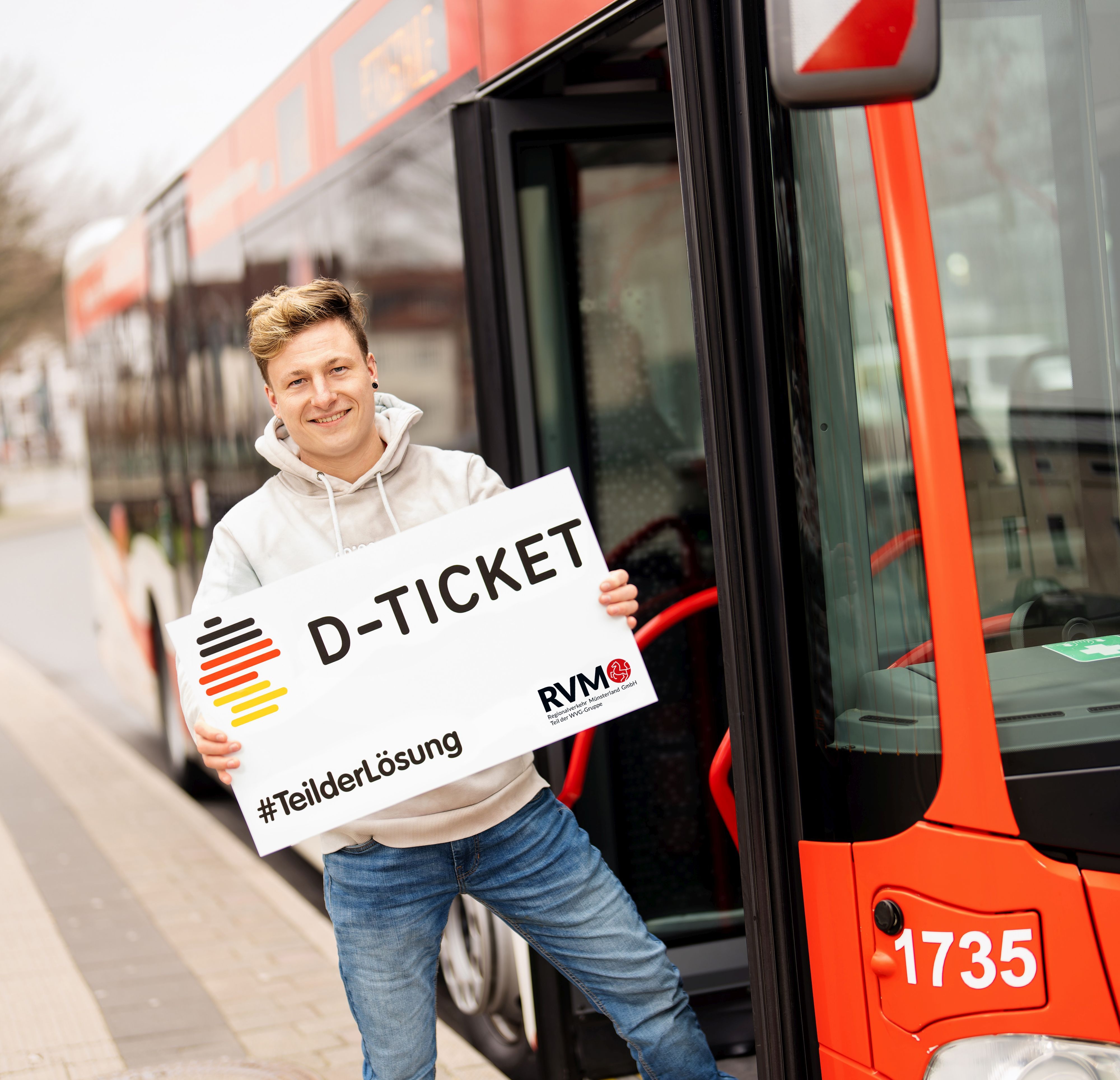 Eine Person steht neben einem Bus mit einem Schild auf dem steht: D-Ticket, #TeilderLösung.