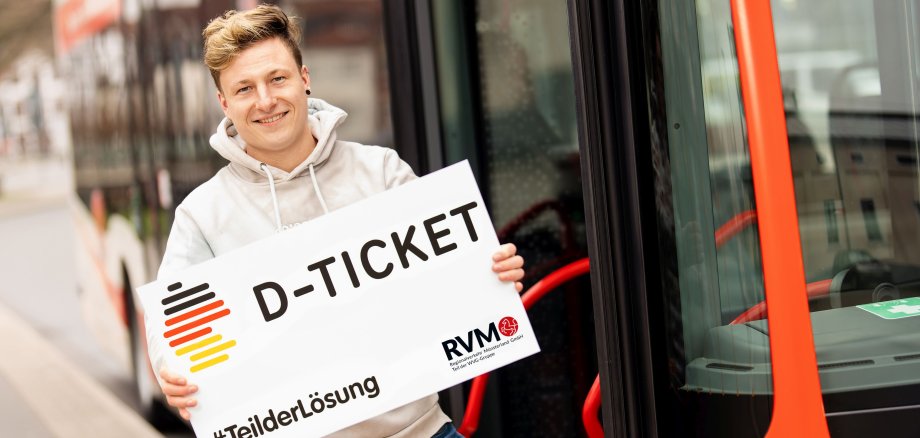 Eine Person steht neben einem Bus mit einem Schild auf dem steht: D-Ticket, #TeilderLösung.