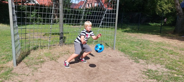Action auf dem Sportplatz: Ein Junge im Tor hält einen Ball.