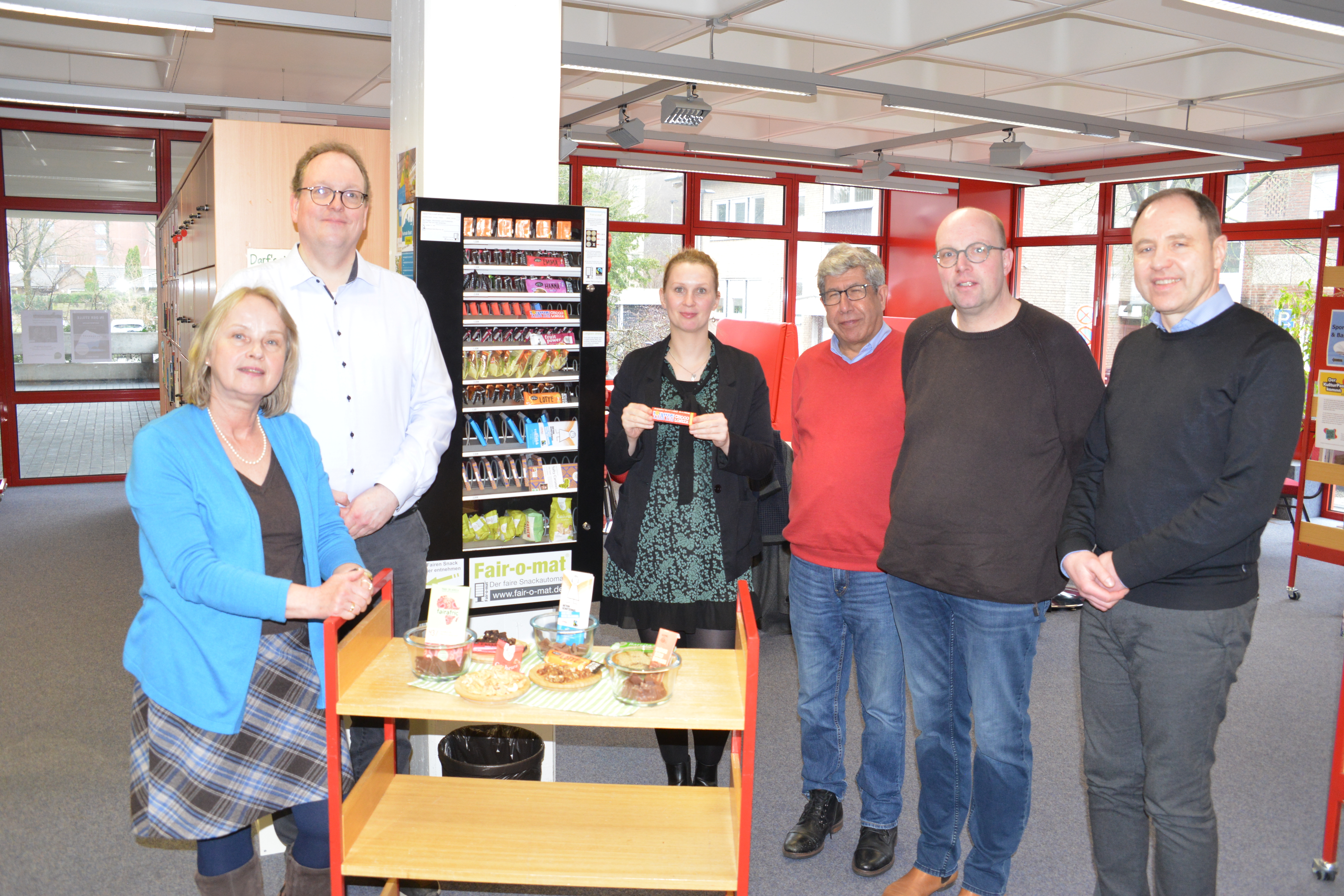 Eine Gruppe von Menschen, die die fairen Snacks aus dem Fairomat im Lesecafé der Stadtbücherei Gronau ansehen