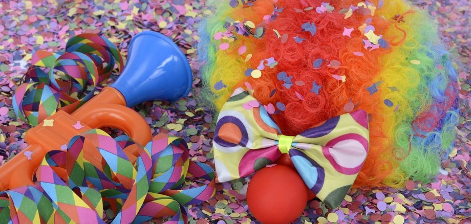 Eine Plastiktröte und eine Clownsmaske weisen auf die geänderten Öffnungszeiten der Stadt Gronau an Altweiber und Karneval hin