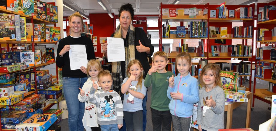 Anne Kammholz von der Stadtbücherei Gronau und Birgit Hüsing-Hackfort vom DRK -Familienzentrum Zum Regenbogenland stehen mit einigen Kindern in der Stadtbücherei, wo ein Kooperationsvertrag beschlossen wurde