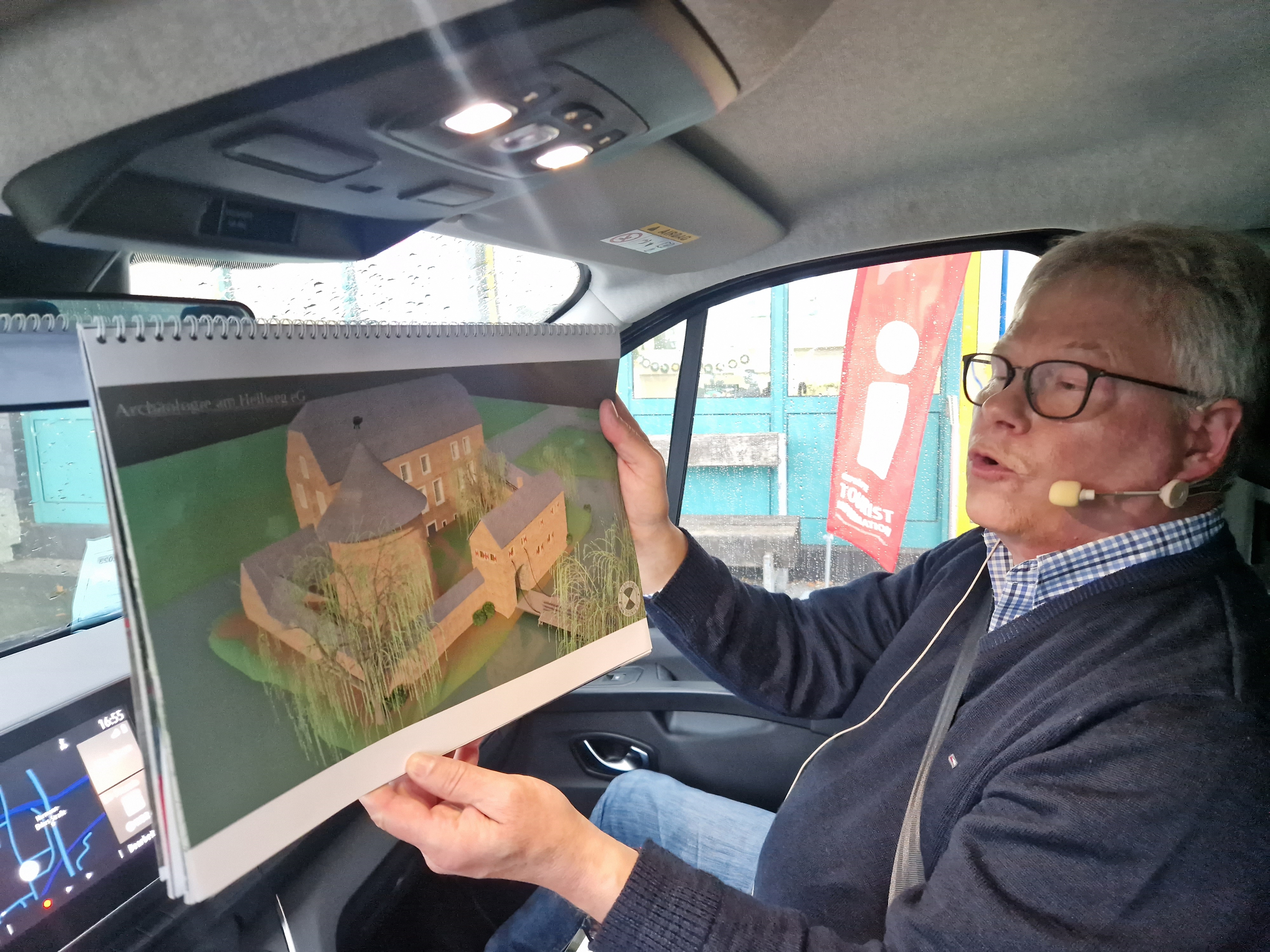 Stadtführer Klaus Wiedau sitzt in einem Bus und deutet auf einen Stadtplan 