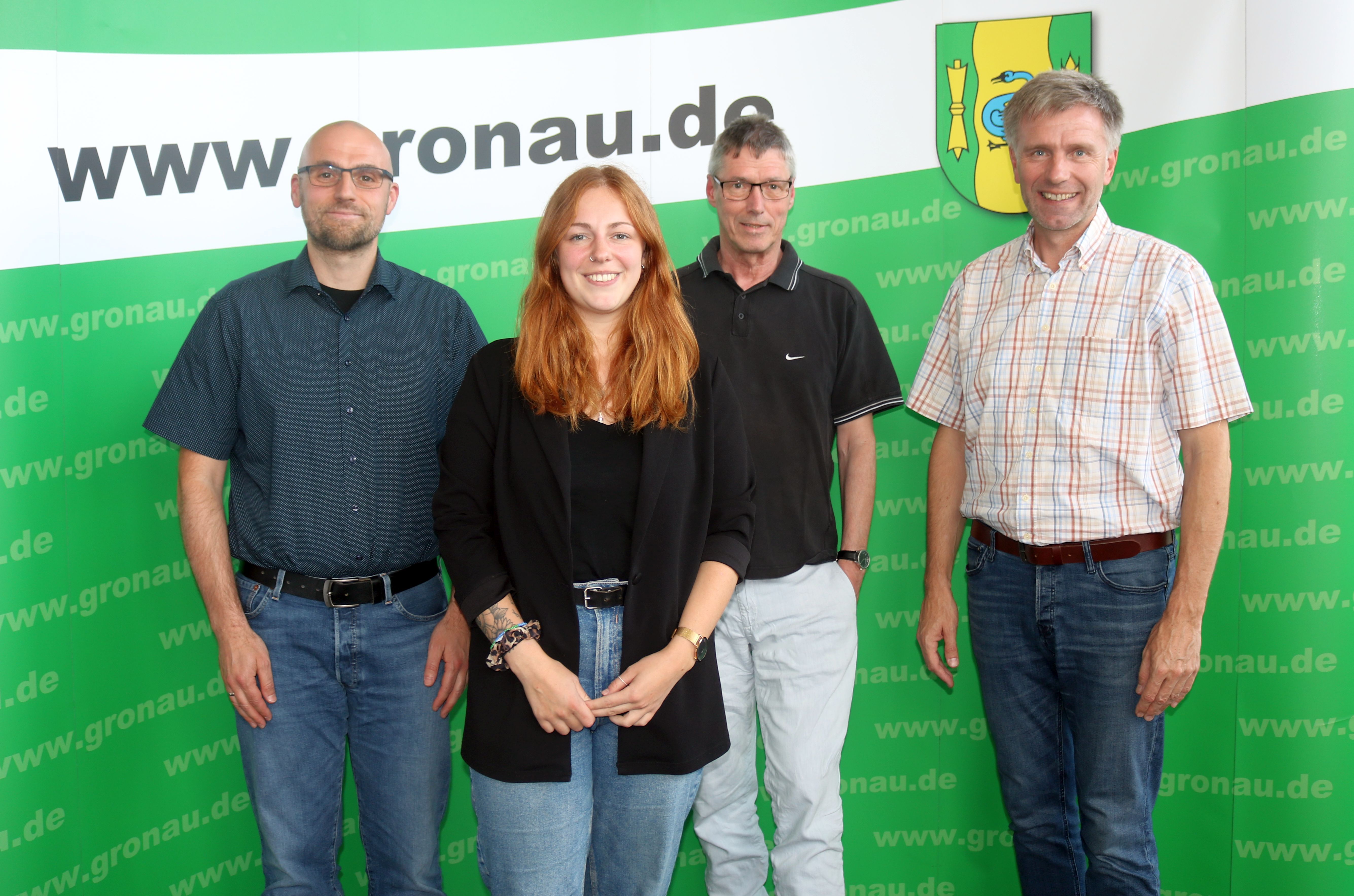 Vertretungen der Caritas und der Verwaltung der Stadt Gronau vor einer grünen Messewand.