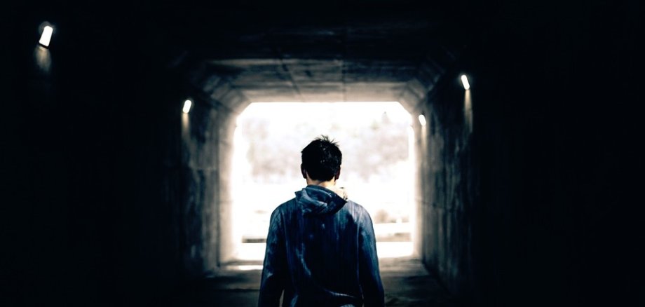 Ein Mensch geht durch einen dunklen Tunnel. Nur am Ende ist etwas Licht zu sehen