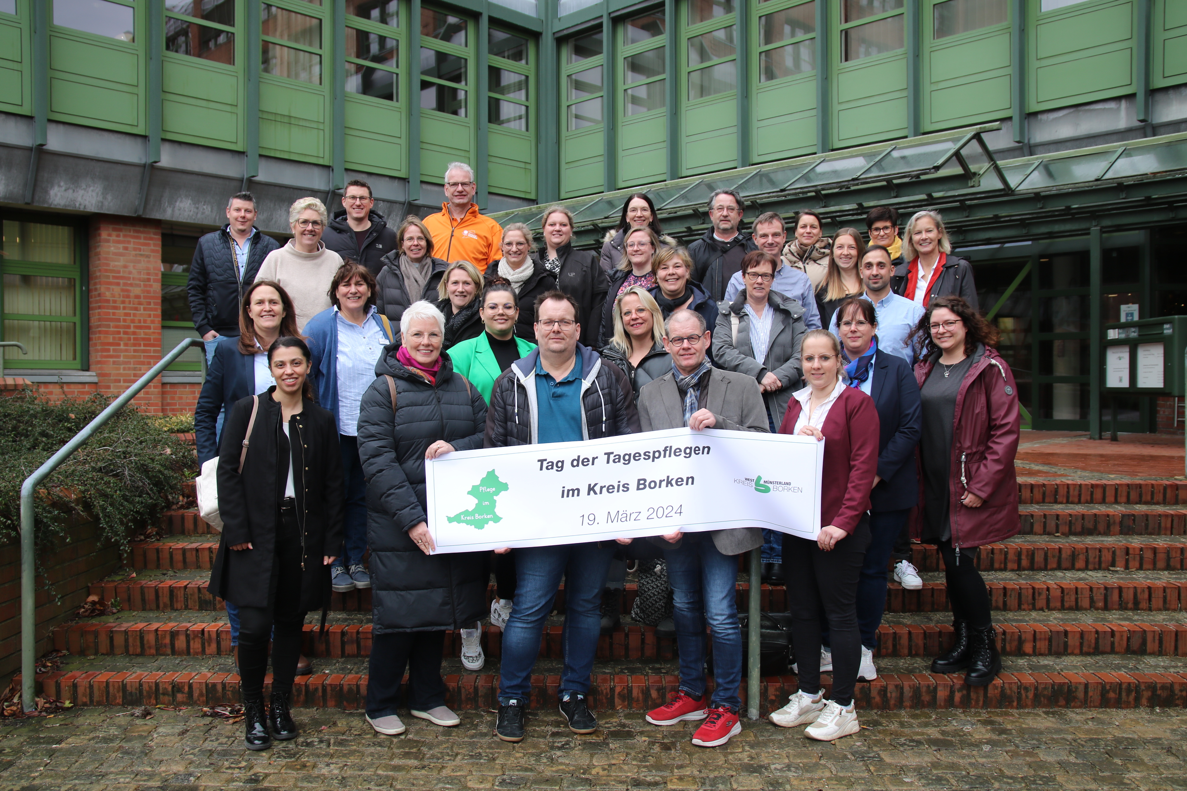 Mitwirkende von Tagespflegeeinrichtungen machen mit einem Plakat Werbung für den 1. Tag der Tagespflege im Kreis Borken. 