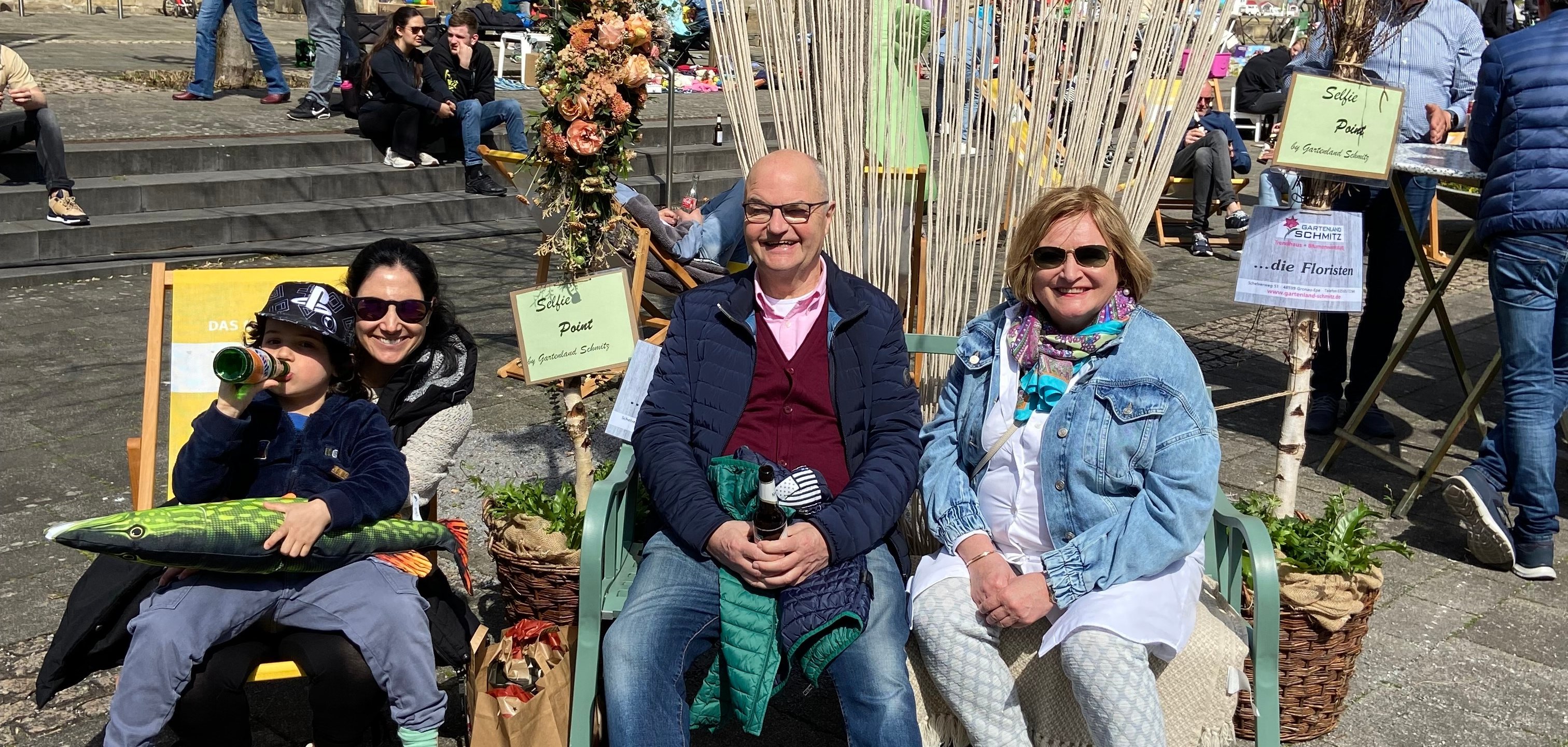 Drei Erwachsene und ein Kind genießen das bunte Treiben im Sonnenstuhl vor der St. Agatha-Kirche