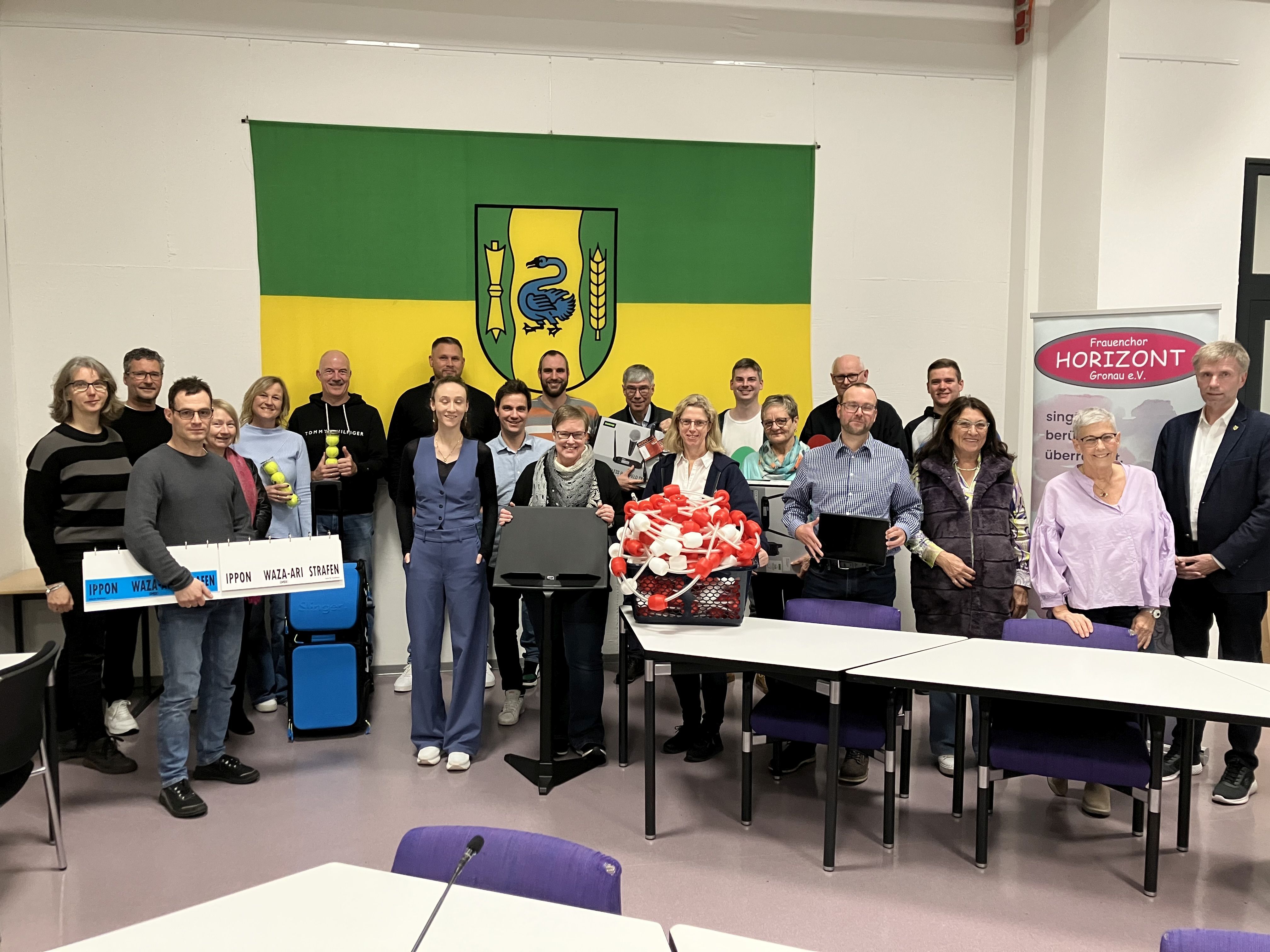 Gruppe von Personen im Ratssaal der Stadt Gronau vor dem Wappen