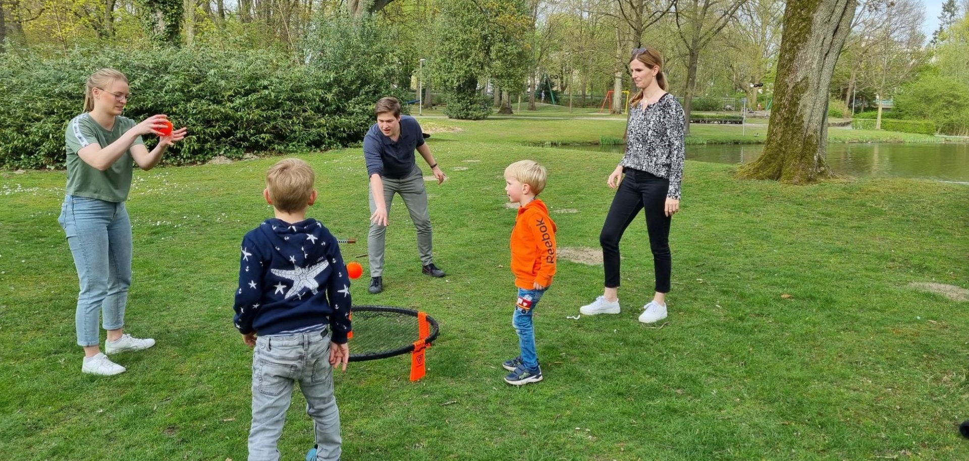 Erwachsene und Kinder spielen ein Spiel mit Bällen auf einer Wiese.
